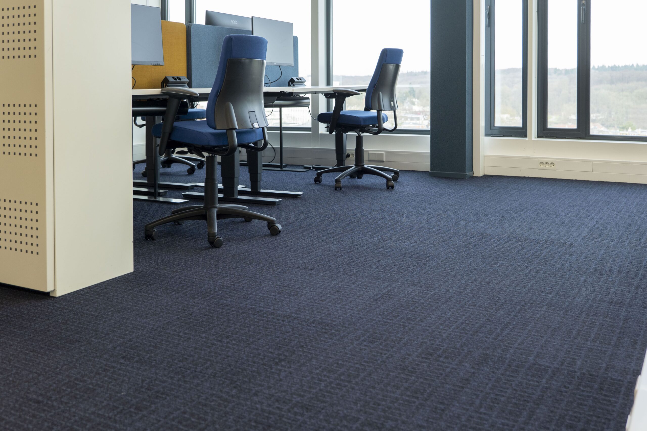 Refurbished blauwe tapijtvloer onder werkplekken bij Witteveen+Bos